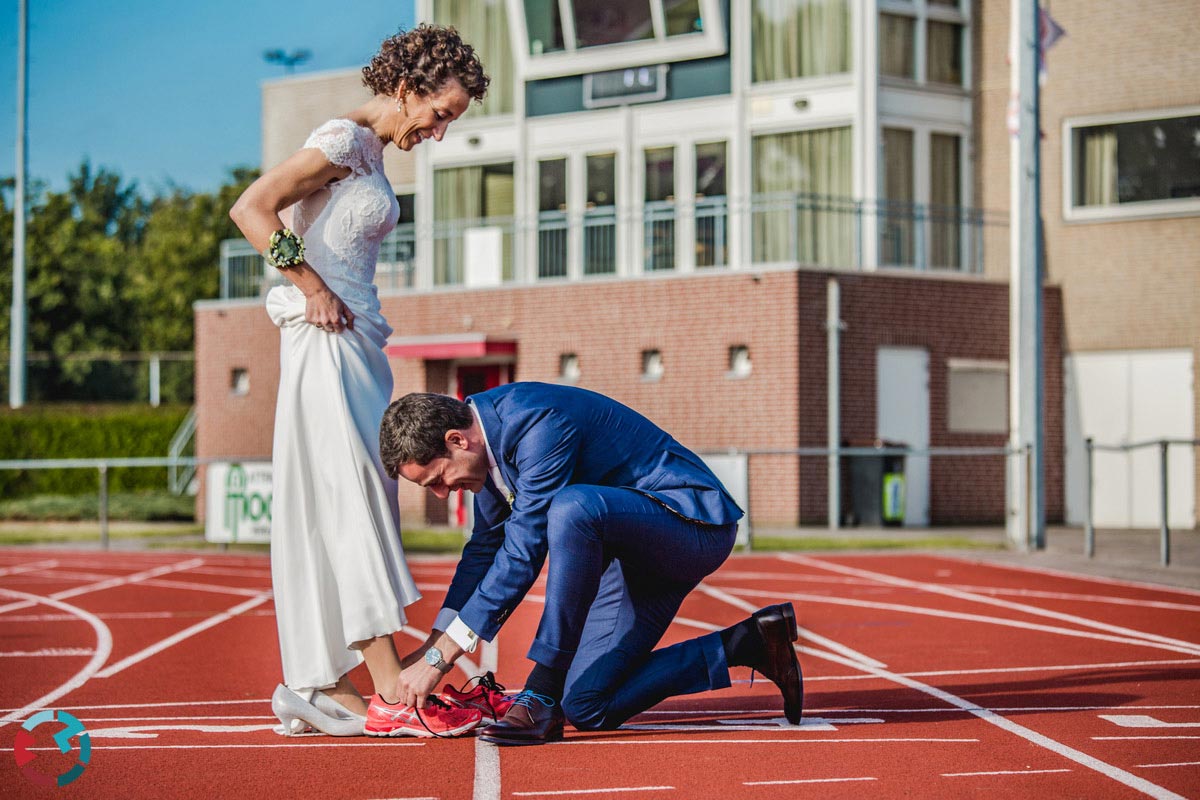 Bruidegom doet running schoenen aan bij bruid op atletiekbaan in Waalwijk