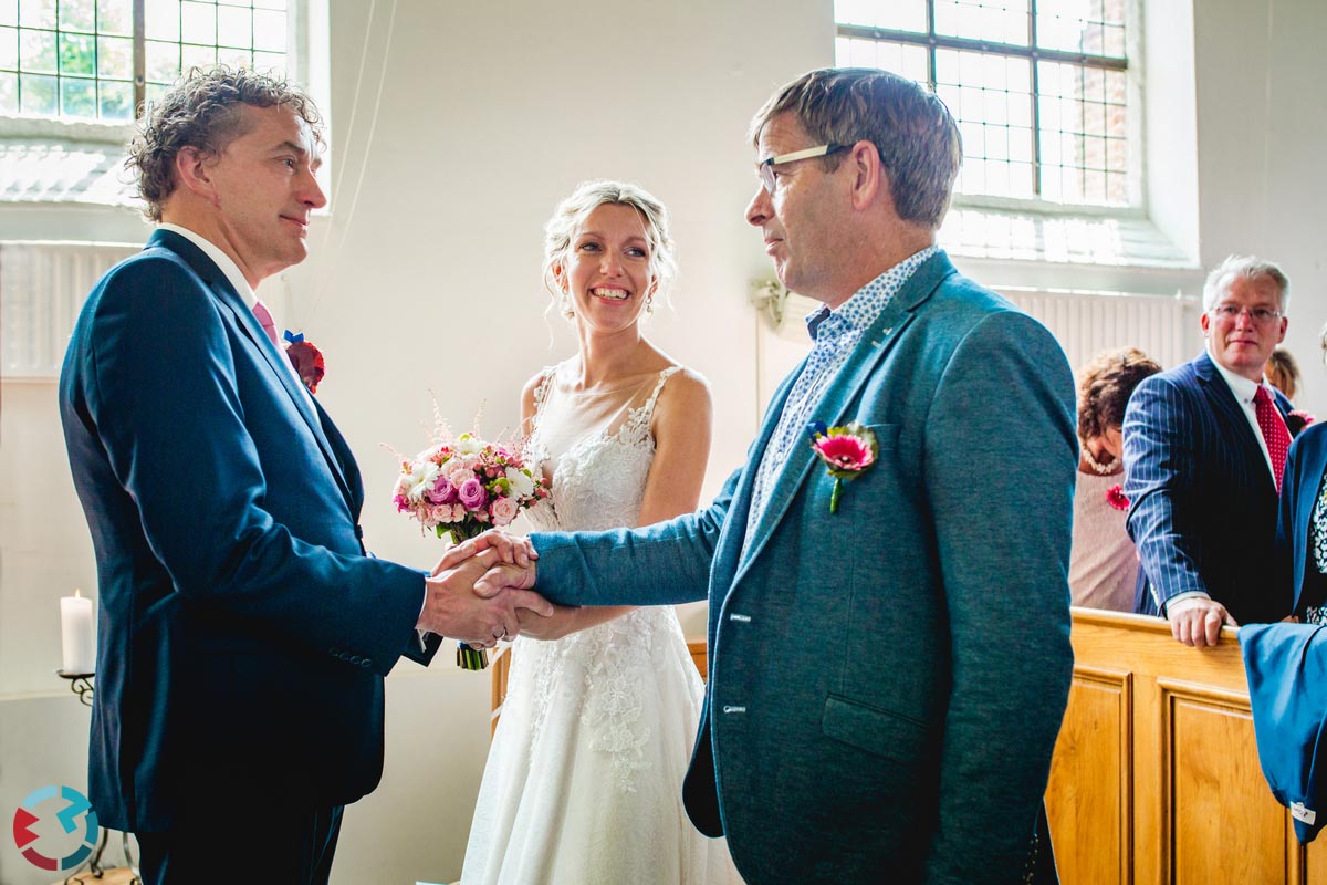 Bruid loopt met haar vader door het middenpad van een kerk.
