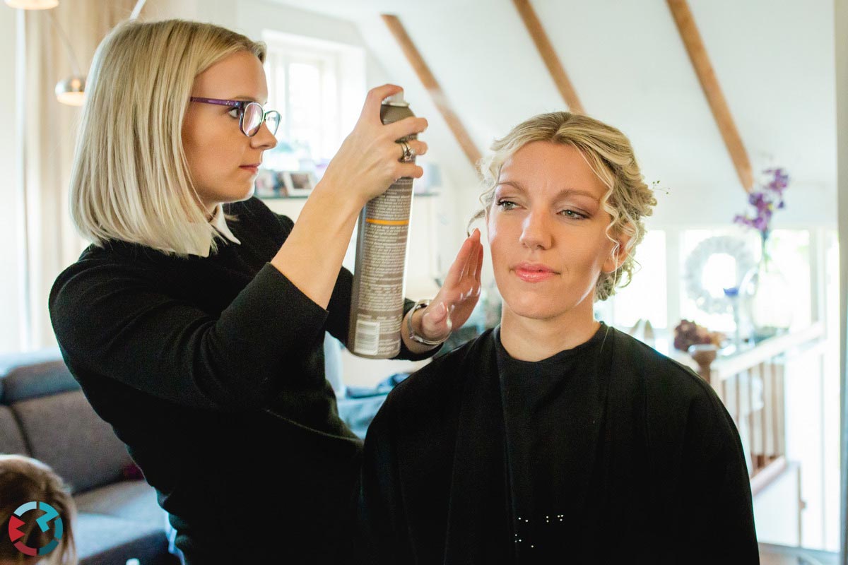 Bruid krijgt haarspray in haar haar.