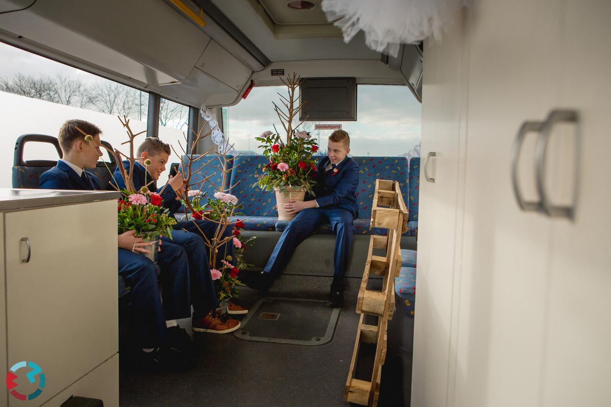 Drie bruidsjonkers met grote bloemstukken achter in een bus