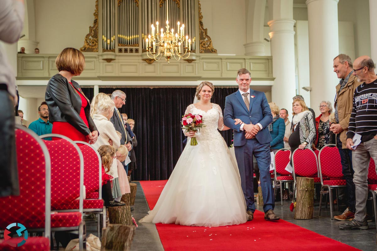 Bruid loopt met vader door middenpad van de Lambertuskerk