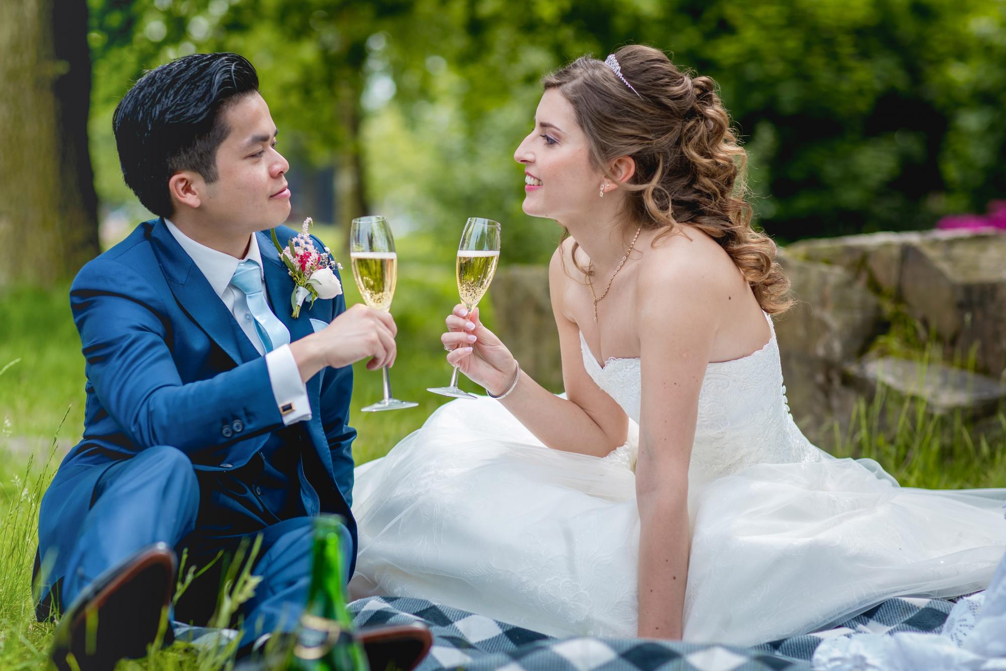 Bruidspaar drinkt samen champagne op een picknickkleed.
