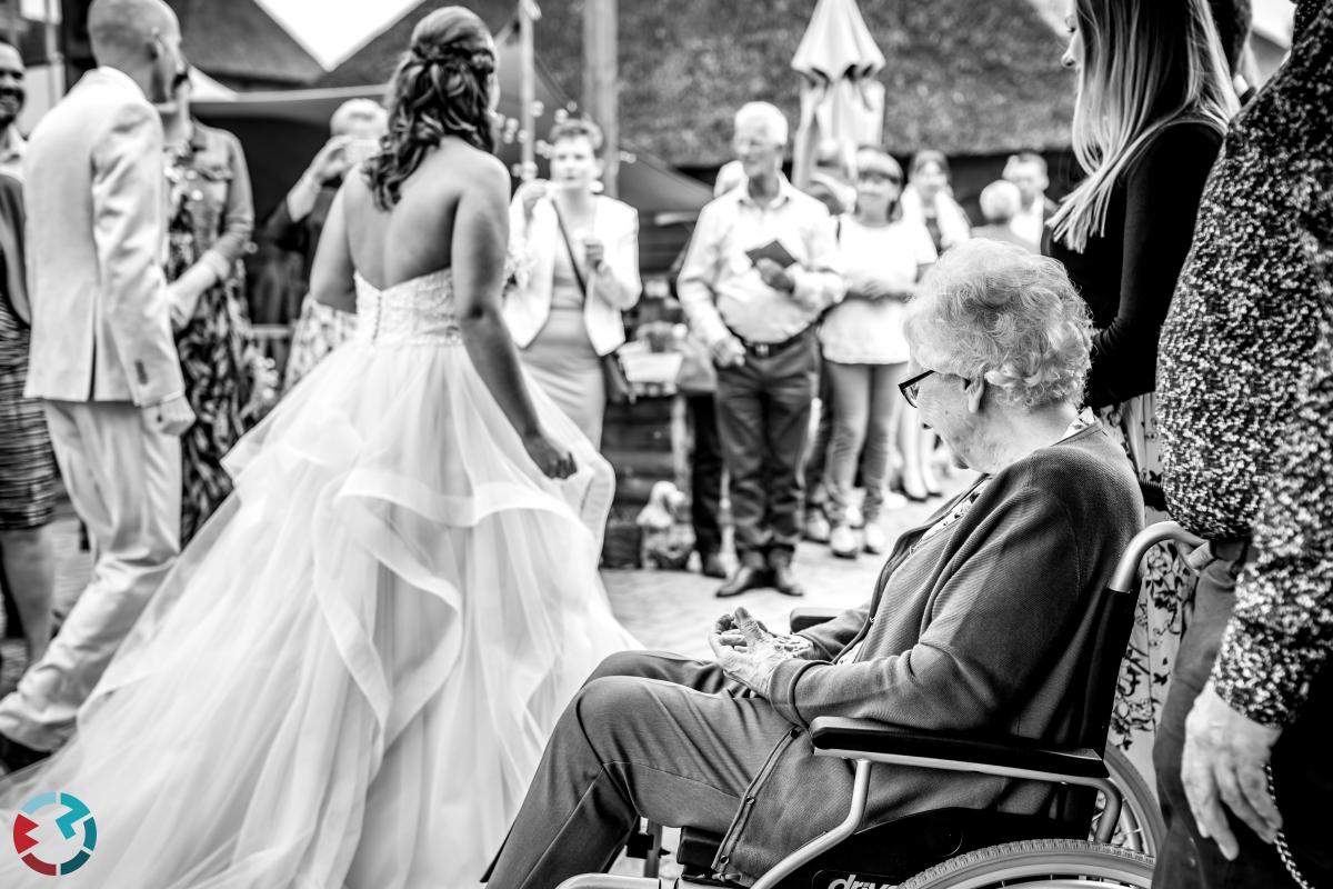 Zwart-wit foto waar een oma in een rolstoel naar de sleep van de trouwjurk kijkt.