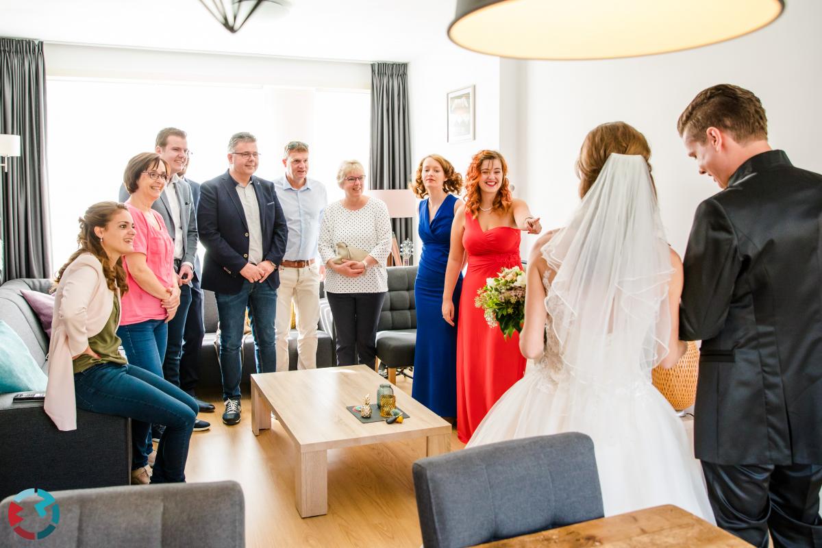 Vrienden en familie bewonderen de bruid en bruidegom in de huiskamer.