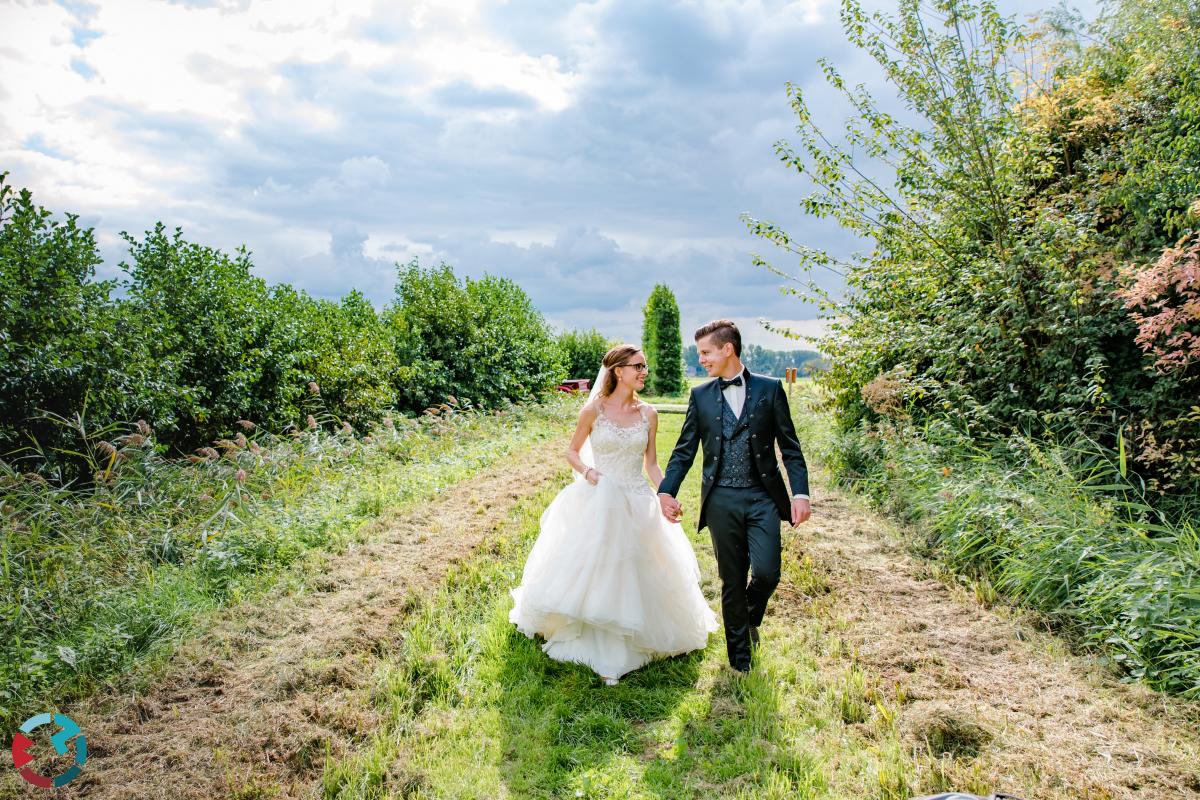 Bruidsreportagefoto van een bruidspaar dat samen over een groen pad lopen.