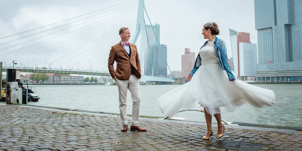 Bruid en bruidegom poseren voor een fotoshoot op een kade in Rotterdam voor de Erasmusbrug