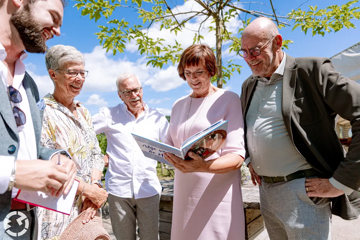 5 mensen kijken lachend in een boek op een zonnige dag.