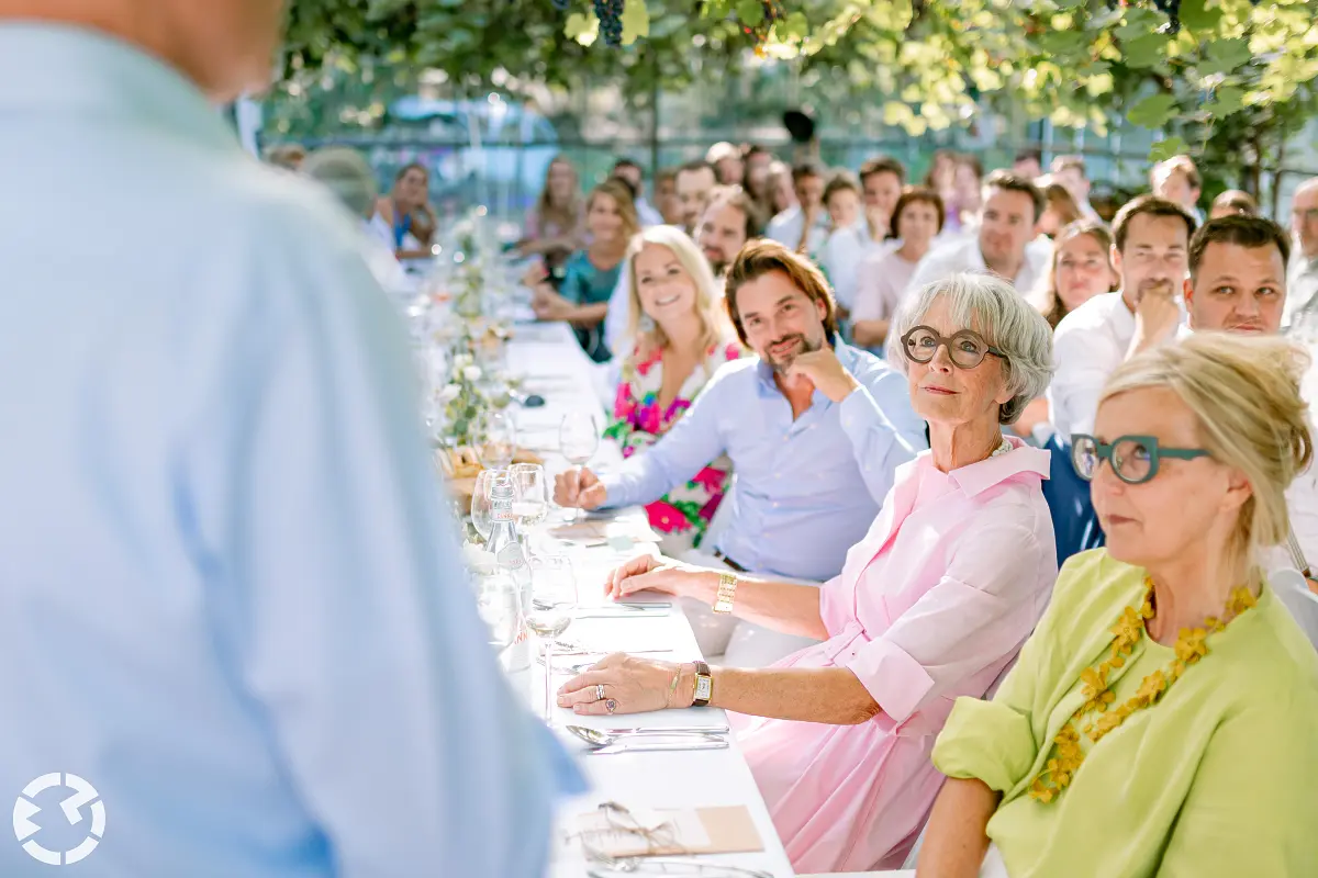 Gasten luisteren naar een speech aan lange tafels in een kast met wijnranken bij De santspuy in etten-leur.