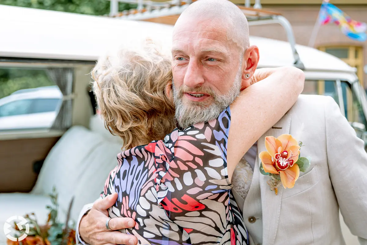 Bruidegom krijgt knuffel van vrouw voor een Volkswagen busje.