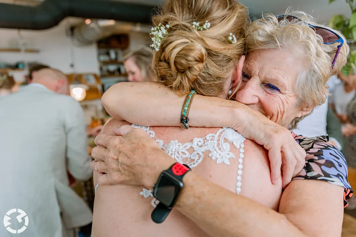 Bruid vanaf achteren gezien die een knuffel van oudere vrouw krijgt.