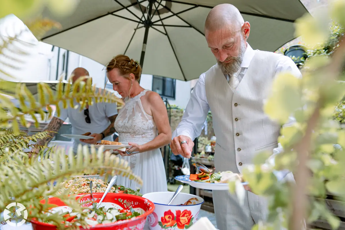 Bruidspaar schept eten op onder een parasol bij JanenAlleman in Breda.