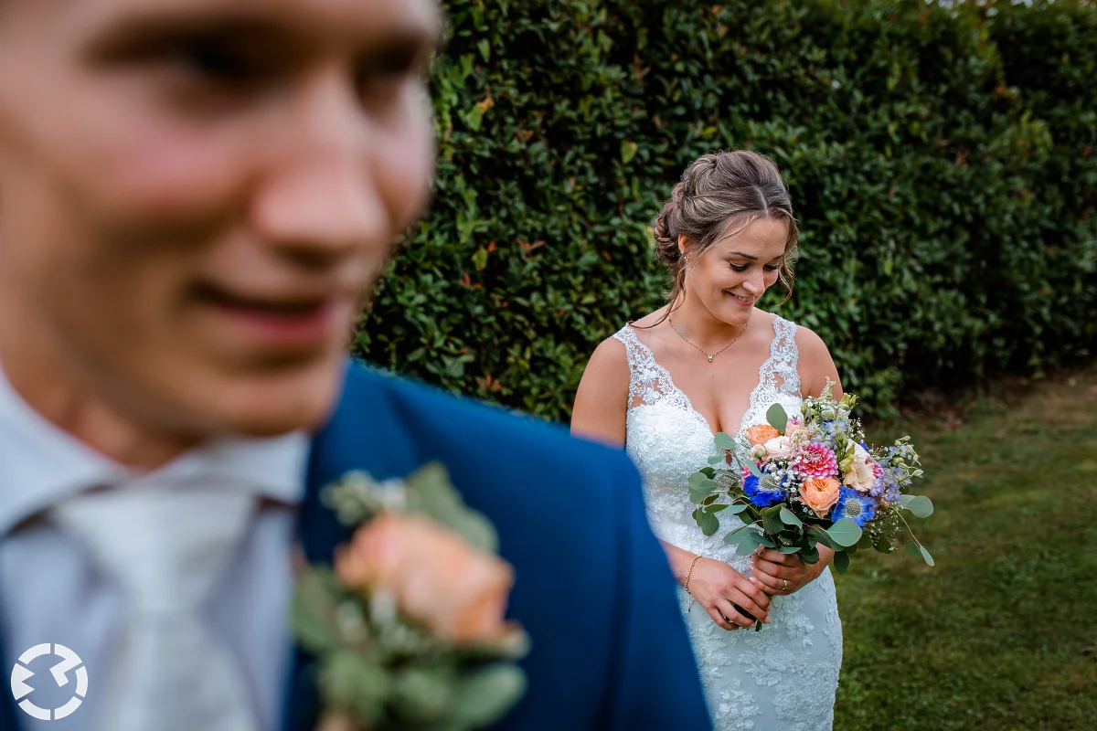 bruid kijkt naar boeket achter de bruidegom die onscherp op de voorgrond zichtbaar is