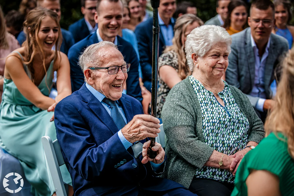 opa lacht en steekt zijn wandelstok omhoog tijdens de ceremonie op de boerderij