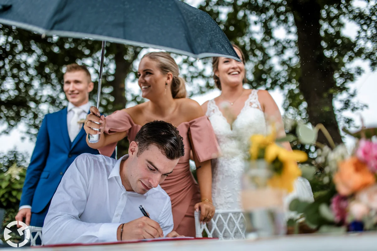 vrouw houdt paraplu boven de getuigen die tekent tijdens de ceremonie op de boerderij