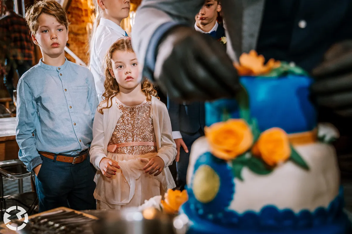 Meisje en jongen kijken volspanning naar de bruidstaart die aangesneden wordt.