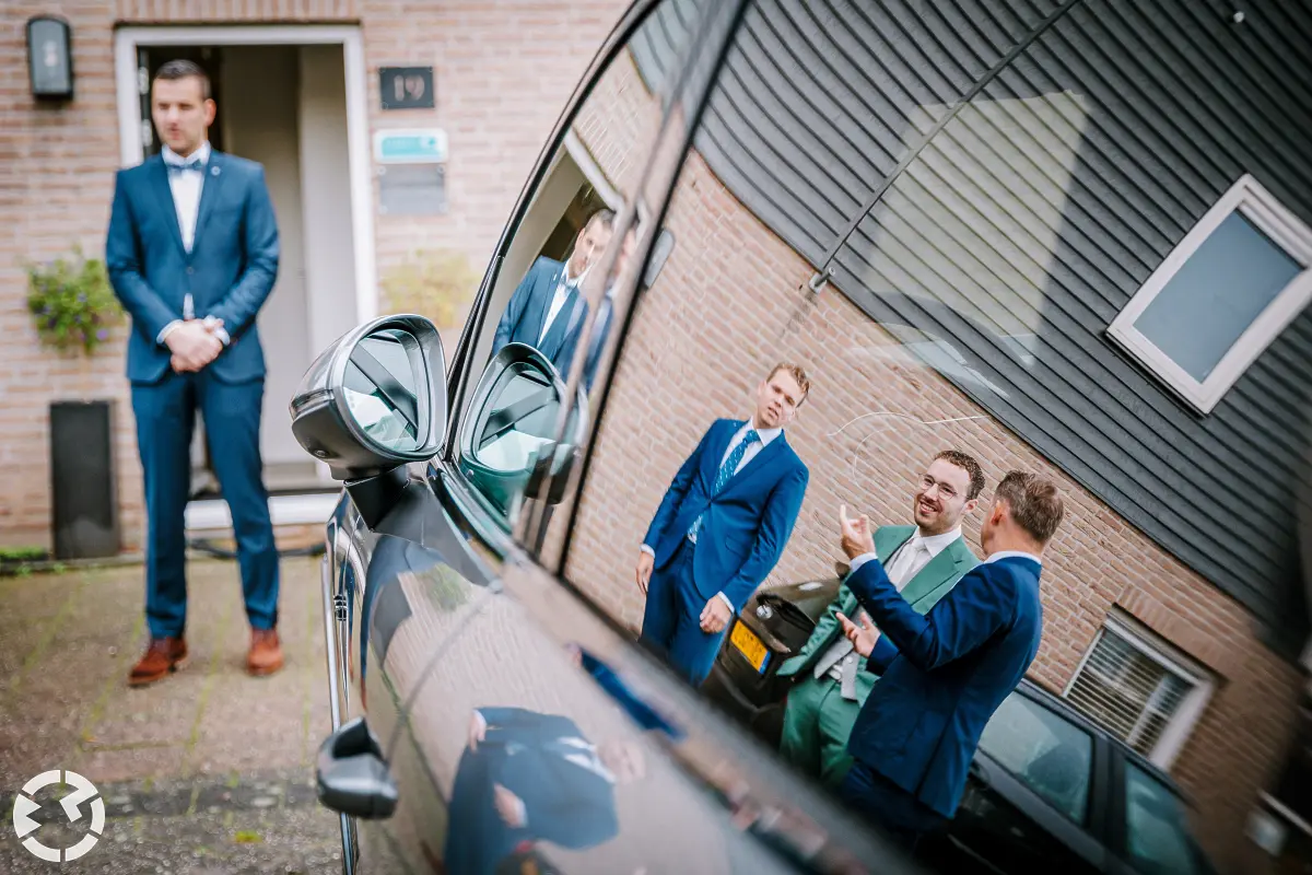 Spiegeling in de zijkant van een auto van de bruidegom en vrienden in pak.