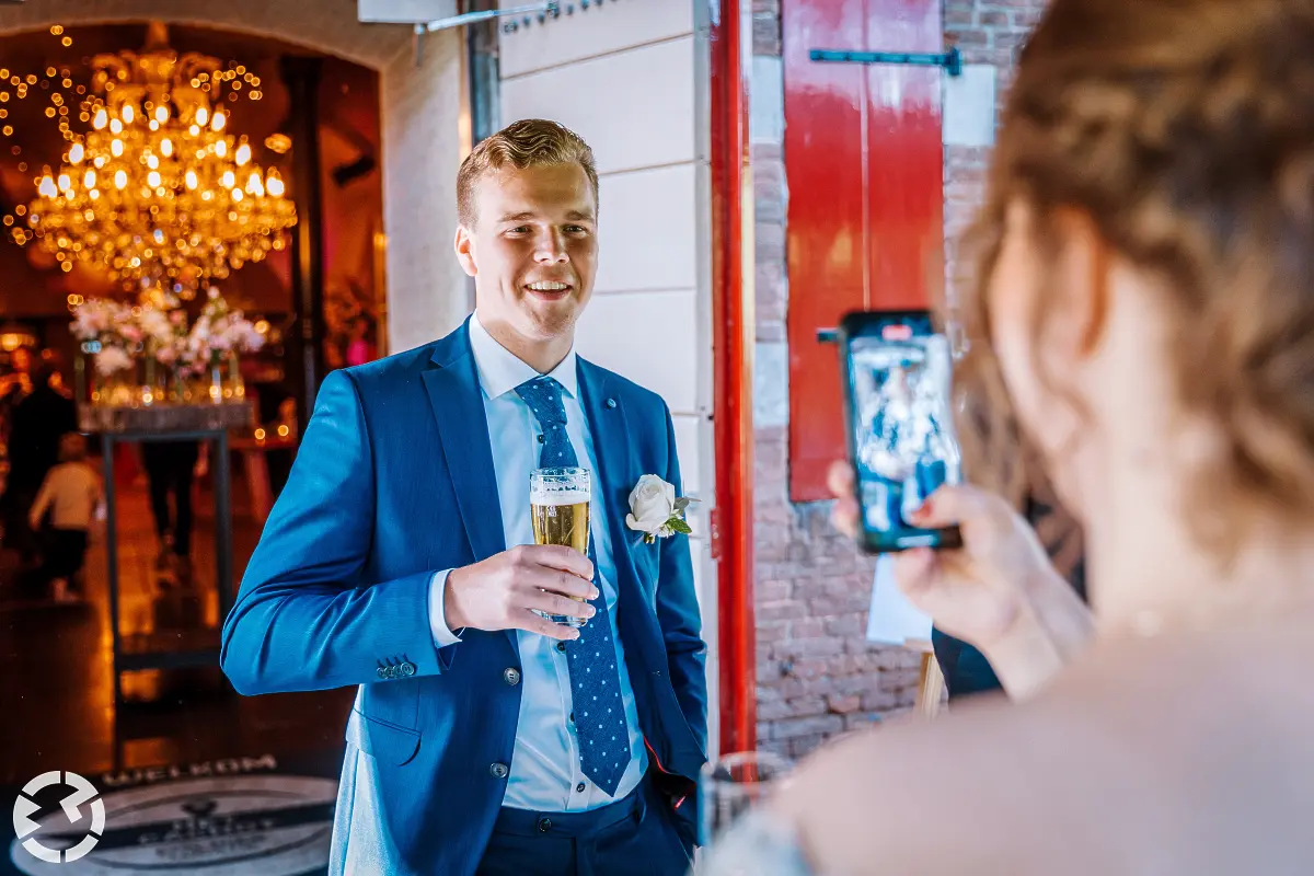 Man met bier wordt voor de deur bij het Cachot in Raamsdonksveer door de bruid gefotografeerd.