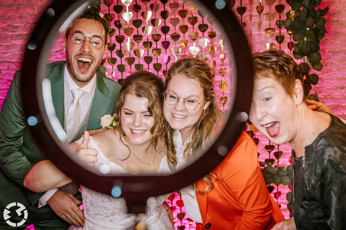 Bruid en bruidegom met 2 gasten poseren vrolijk voor een photobooth