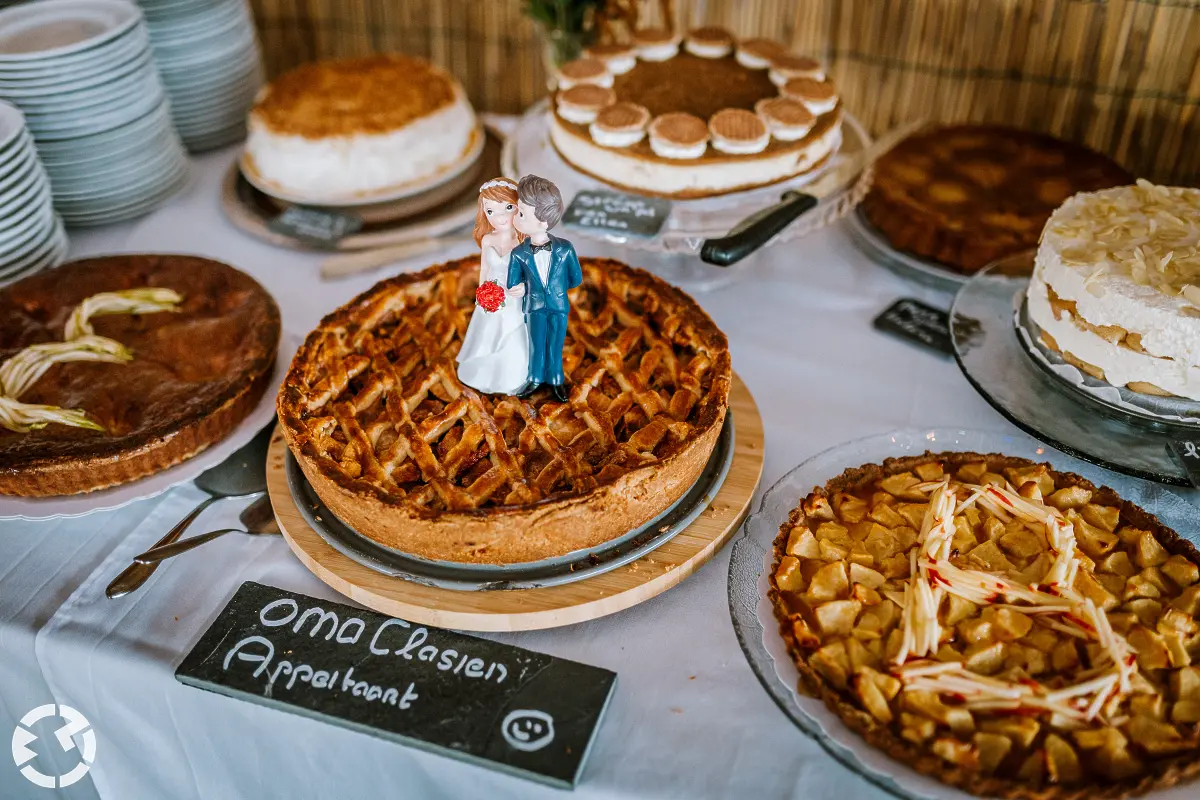 Verschillende taarten op een tafel, de appeltaart van oma heeft een topper van een bruidspaar erop.