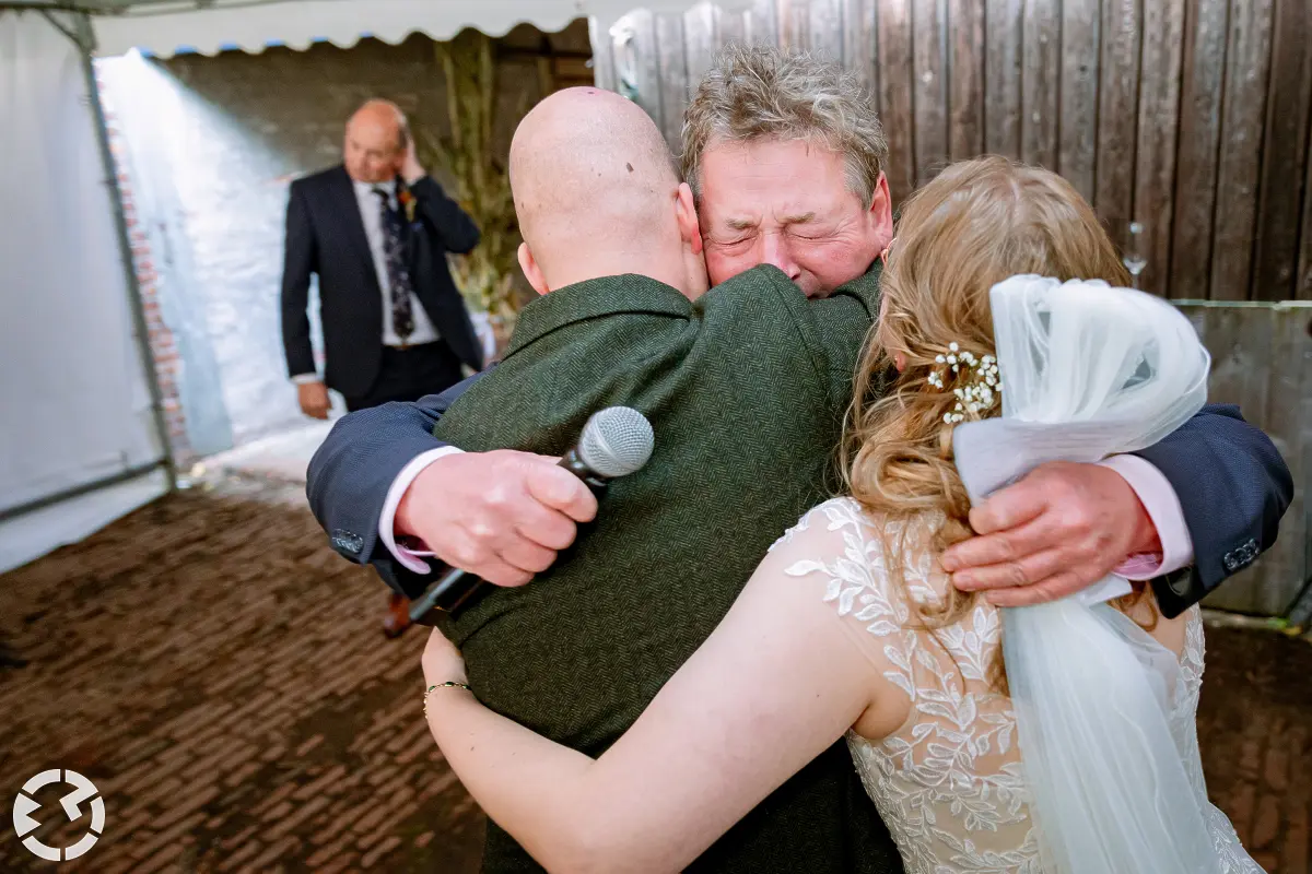 Vader van de bruid omhelst het bruidspaar emotioneel na zijn speech.