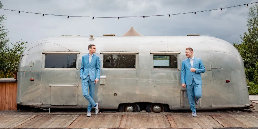 2 bruidegommen staan voor een oude camper bij Het Houtse Meer