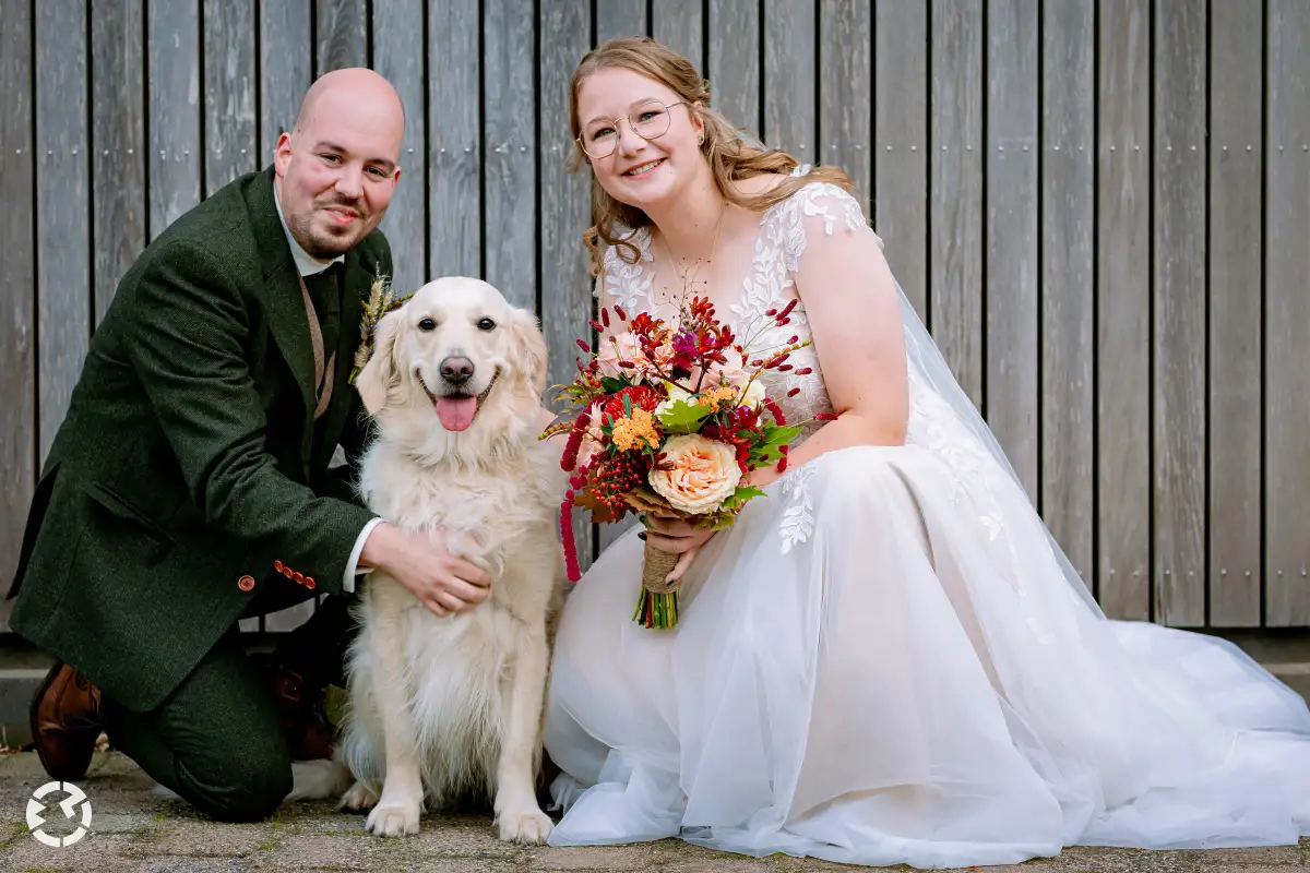 Bruidspaar geknield naast een golden retriever.
