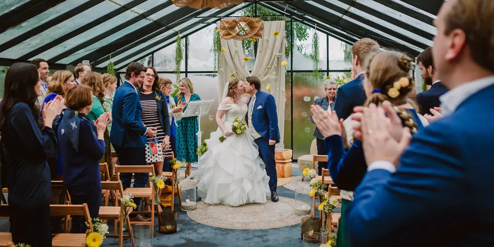 Bruidspaar geeft elkaar een kus tijdens de ceremonie met 2 trouwfotografen
