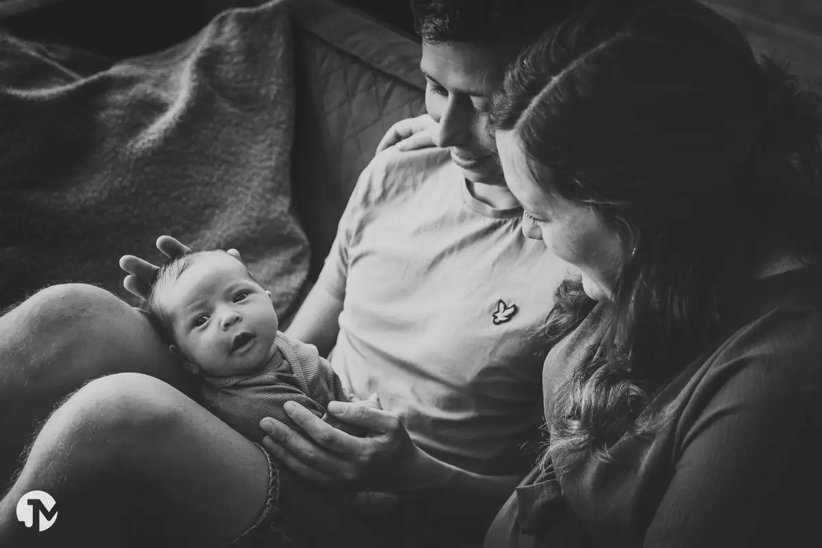 Pasgeboren meisje zit met haar ouder op de bank tijdens lifestyle babyshoot