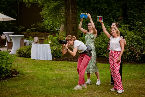 3 vrouwen proberen achter de fotograaf aandacht te trekken aan de kinderen die op de foto moeten.