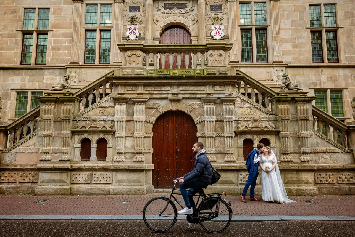 Bruidspaar kust elkaar voor het stadhuis van Leiden terwijl een fietser voorbij komt.
