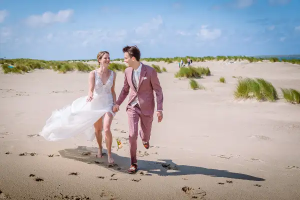 Bruidspaar rent over het strand tijdens hun bruidsreportage.