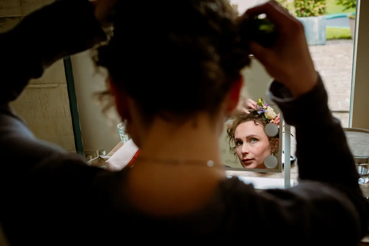 Bruid doet bloemen haarstukje in voor de spiegel.