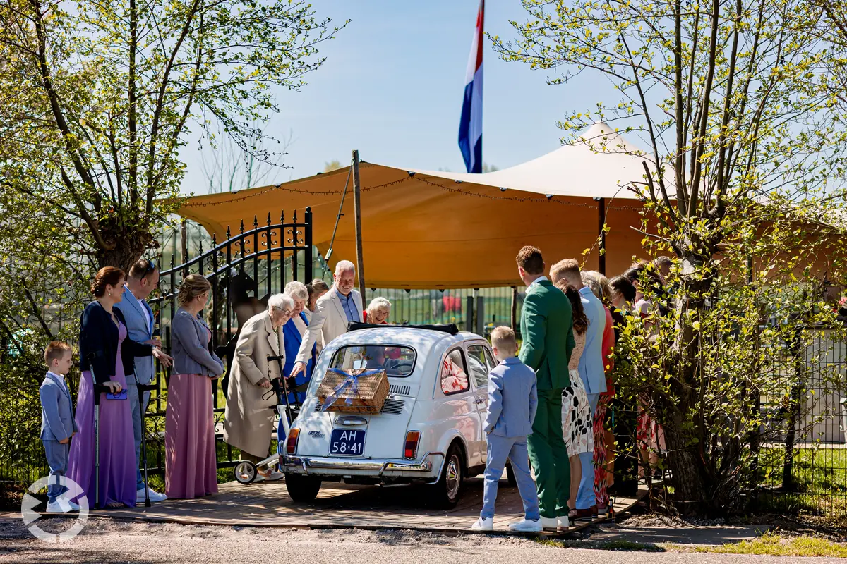 Aankomst van bruidspaar in kleine Fiat als trouwauto.
